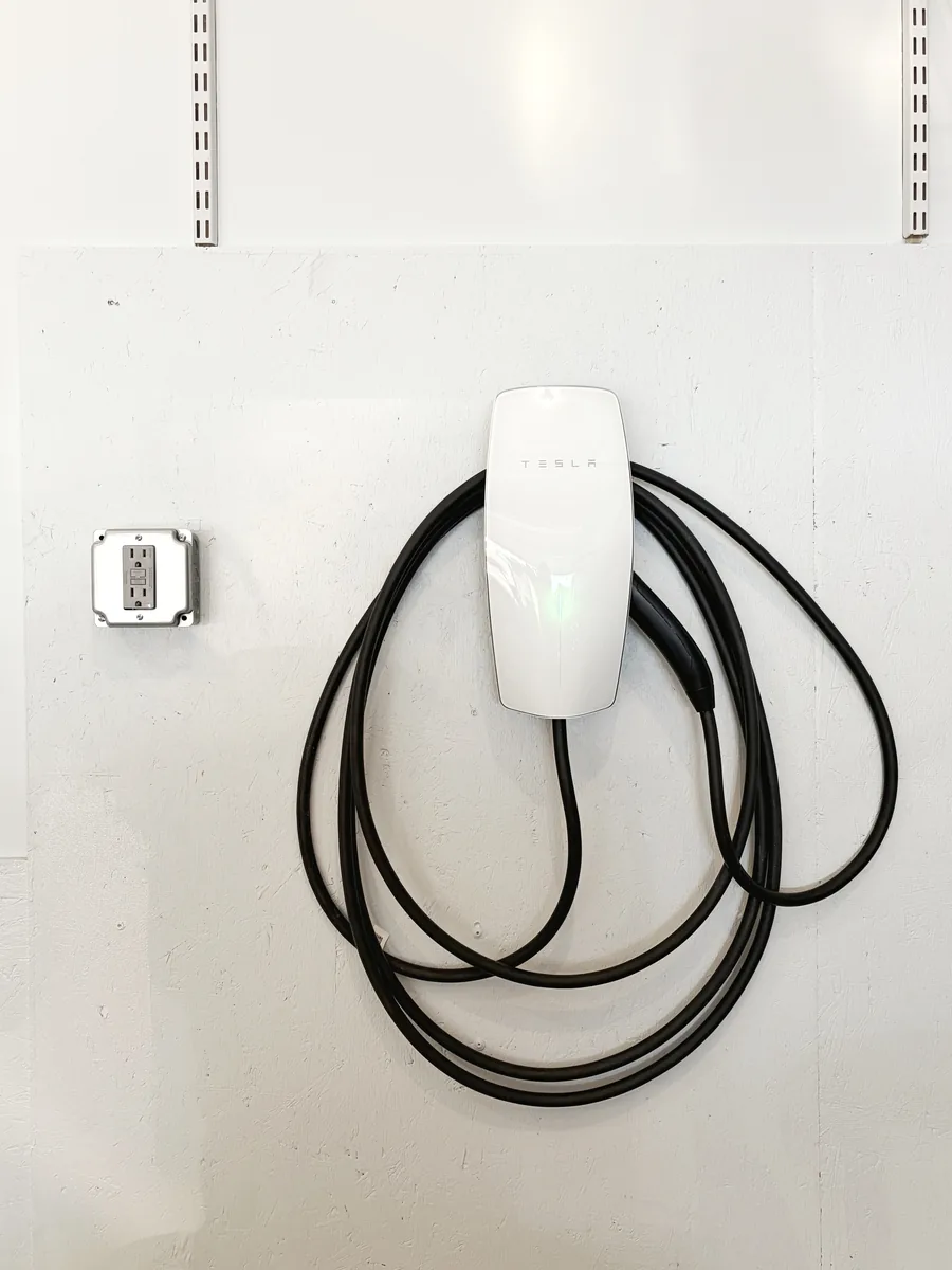 Finished Tesla Wall Connector on the painted Boalsburg garage wall, cable coiled, with the existing GFCI receptacle alongside